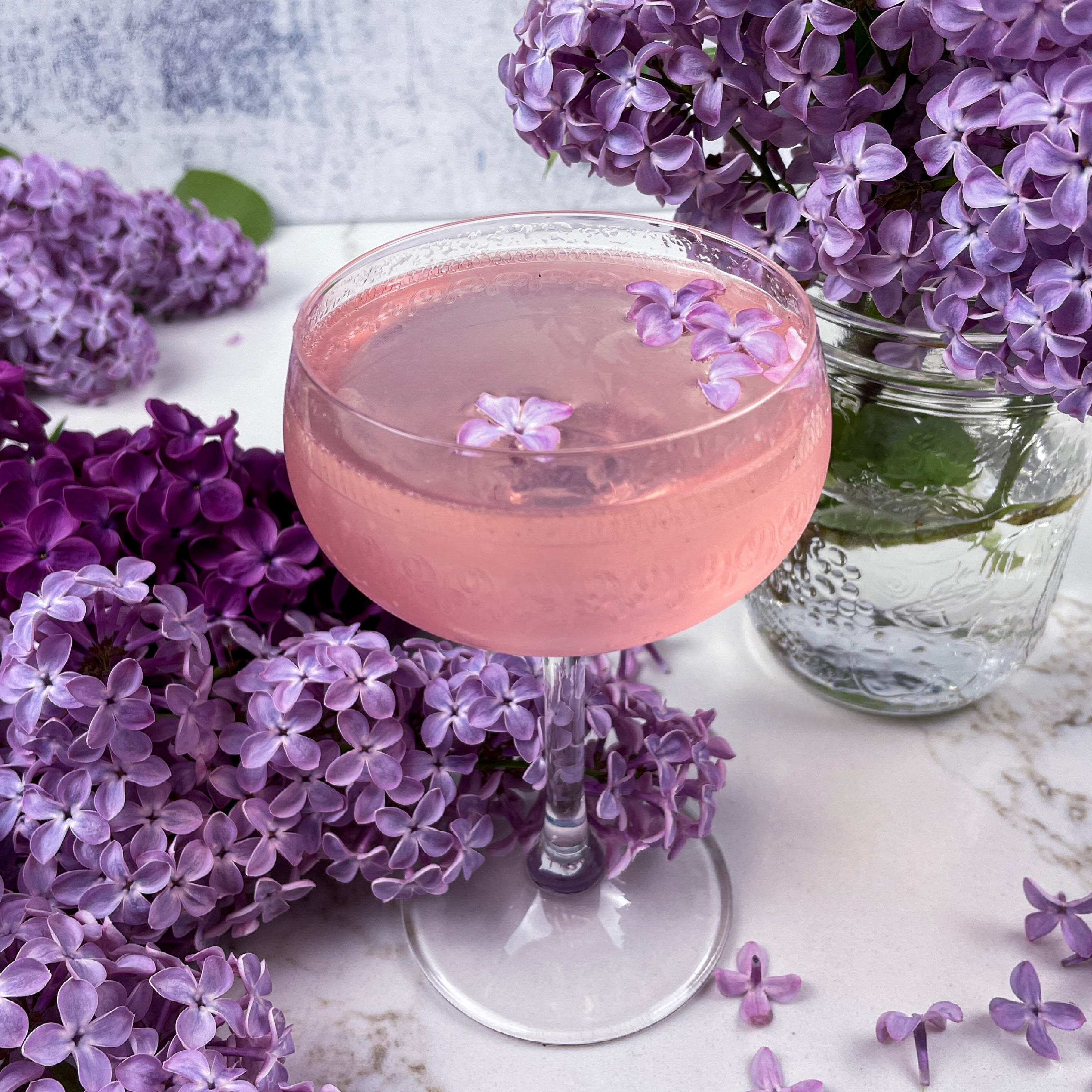 Lilac French 75 in a coupe glass surrounded by lilacs