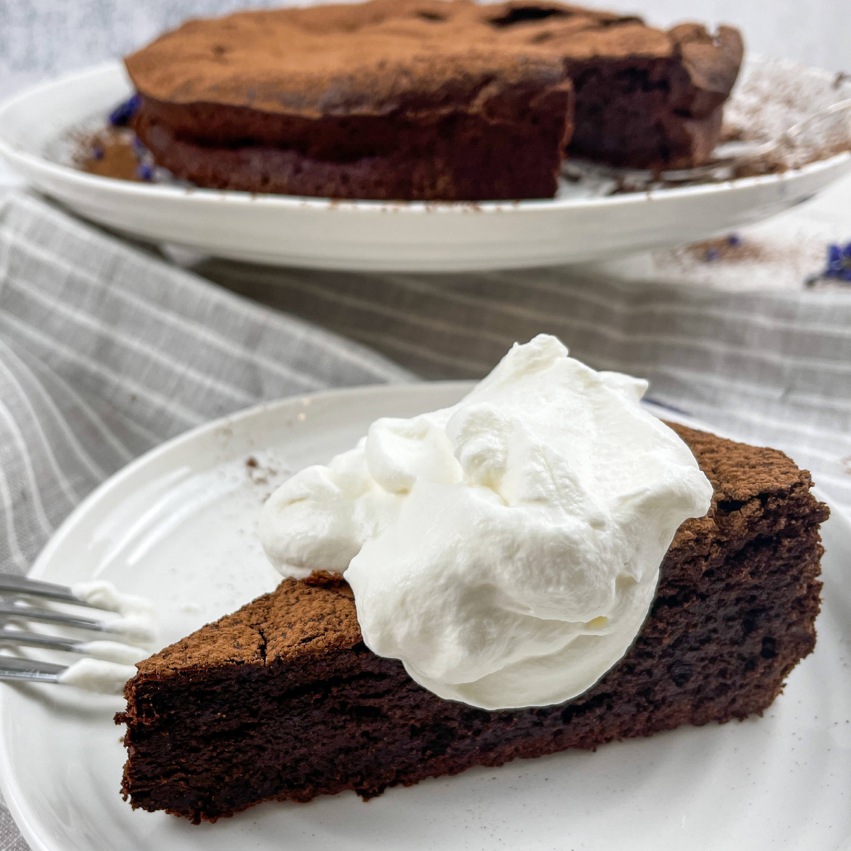 Slice of flourless chocolate cake topped with whipped cream