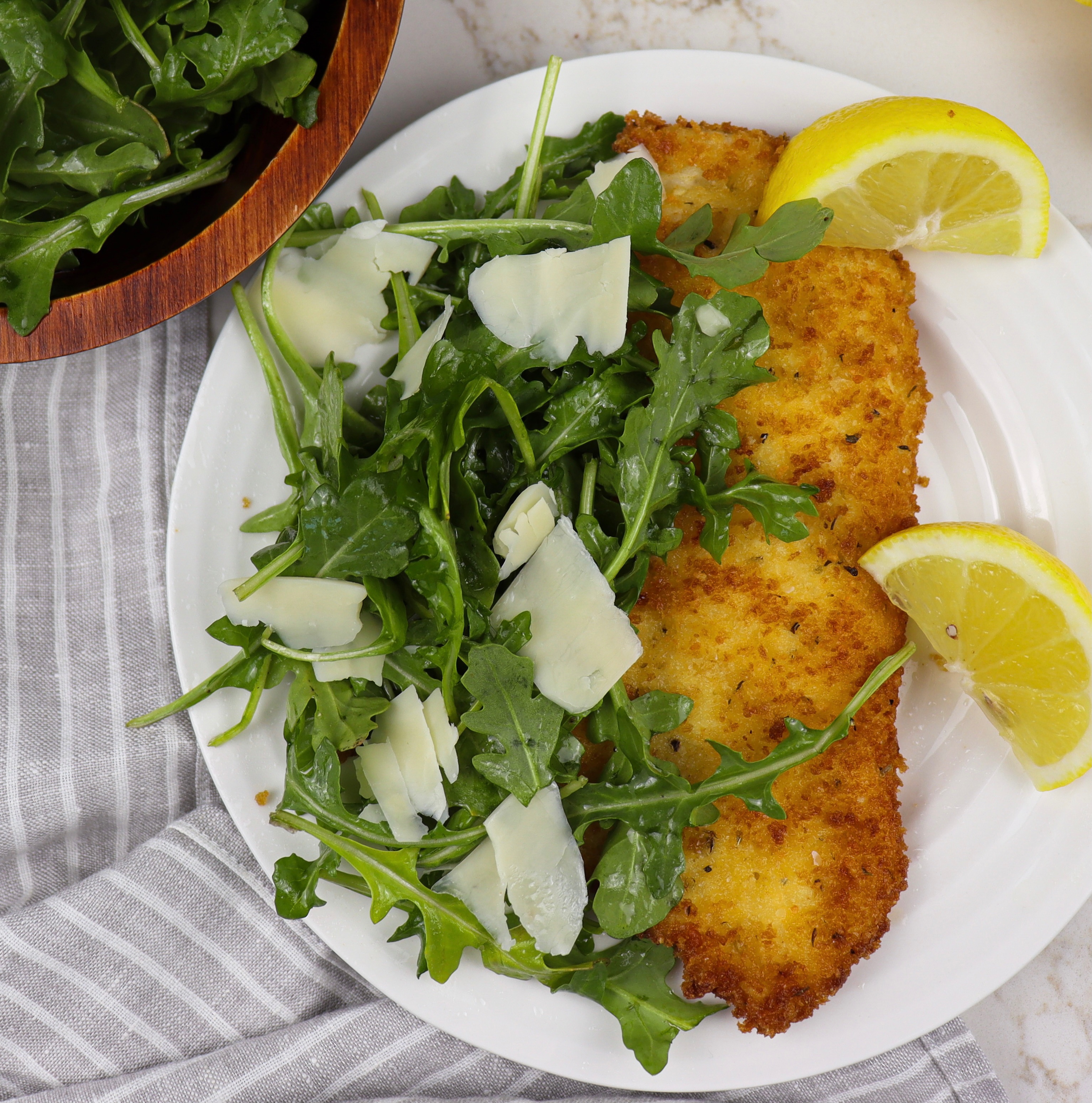 Plate of chicken milanese with side of arugula salad