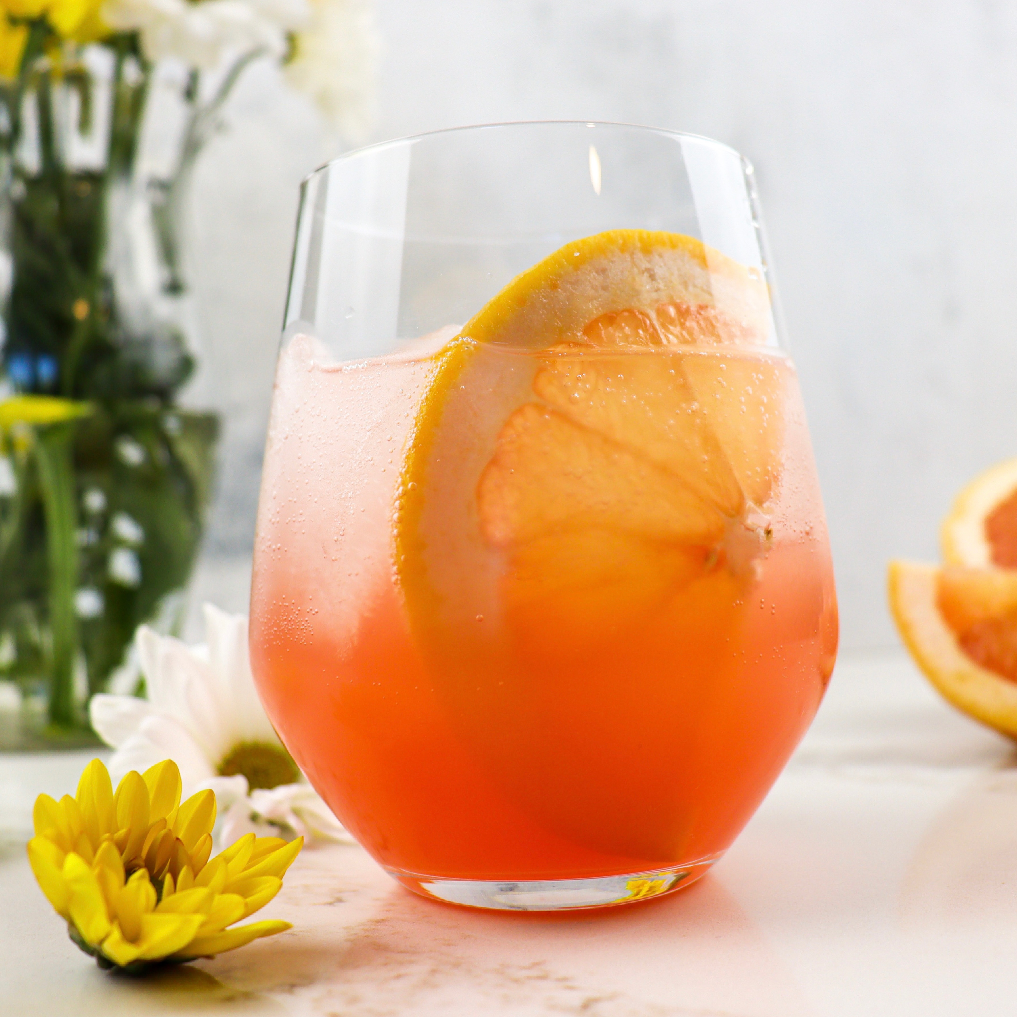 Tumbler of Elderflower Grapefruit Spritzer with flowers in the background
