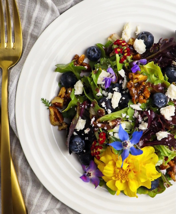 Plate of blueberry salad topped with edible flowers