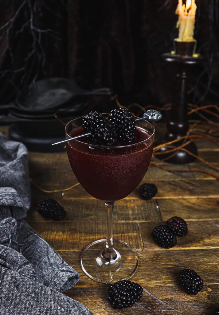 A cocktail glass filled with liquid topped with blackberries