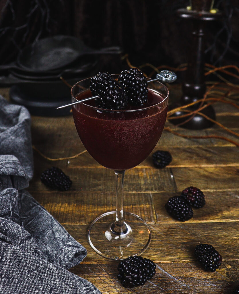 A cocktail glass filled with liquid topped with blackberries