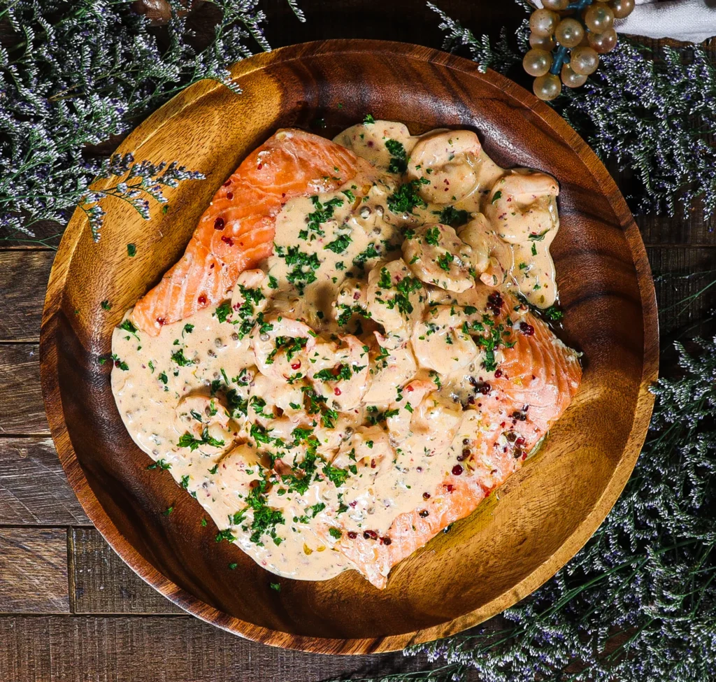 View from above of salmon topped with shrimp and a pink peppercorn cream sauce