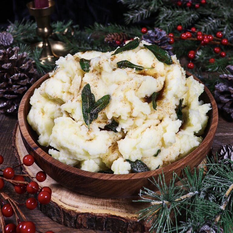 mashed potatoes with crispy sage and browned butter in a rustic bowl surrounded by winter greenery