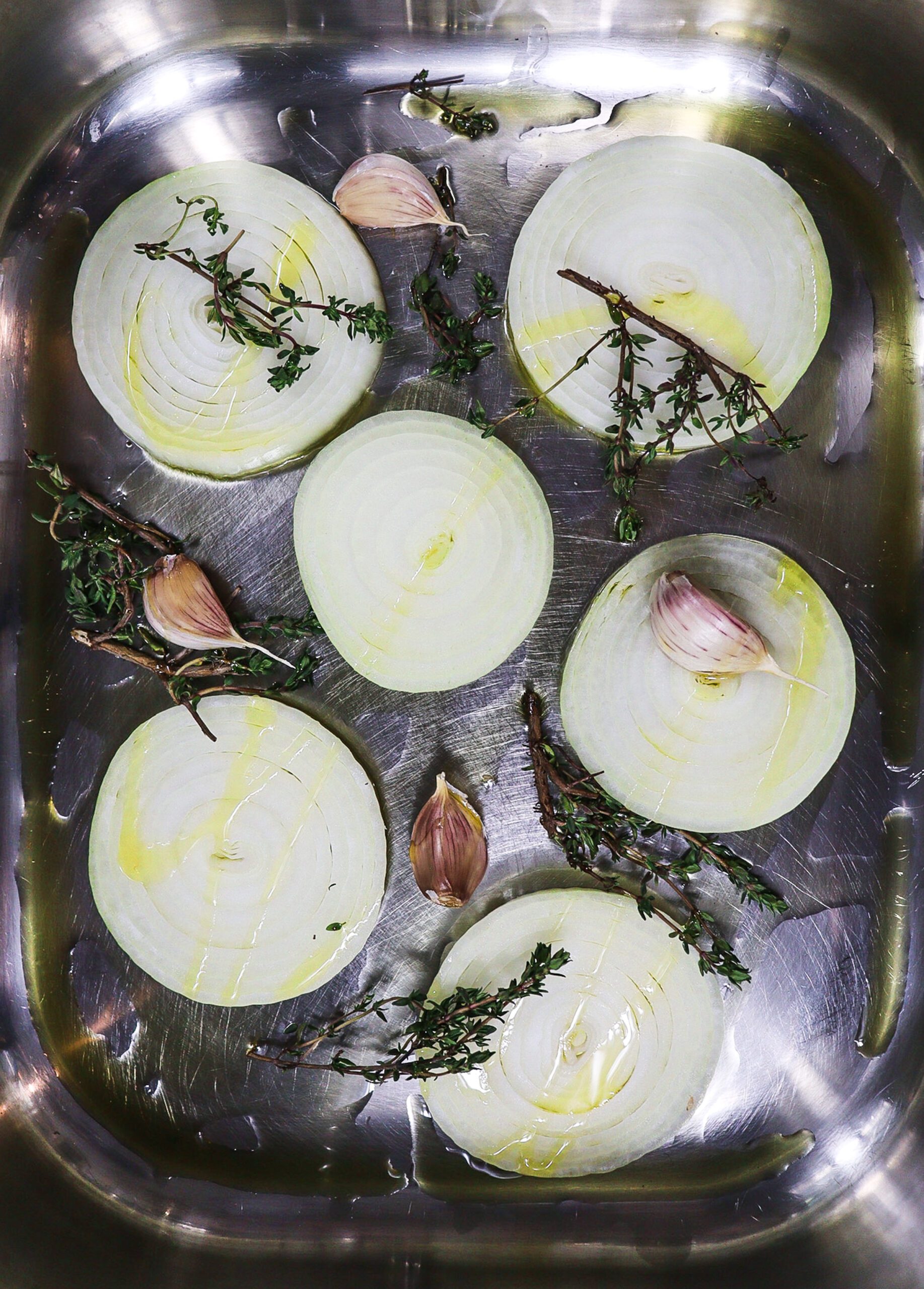 Bottom of roasting pan with onion slices, garlic cloves, thyme and olive oil