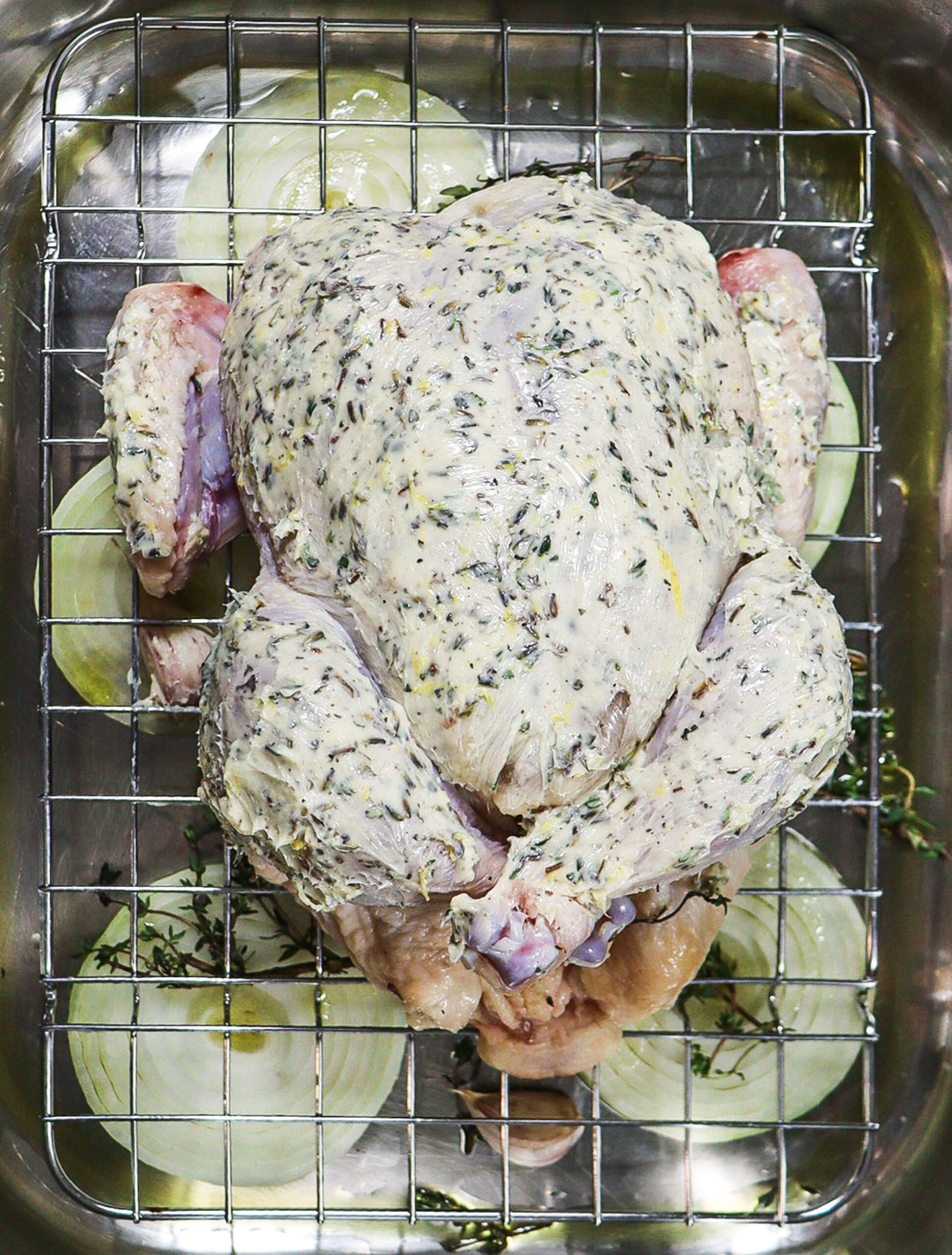 Roasting pan with aromatics and roast chicken covered in compound lavender butter