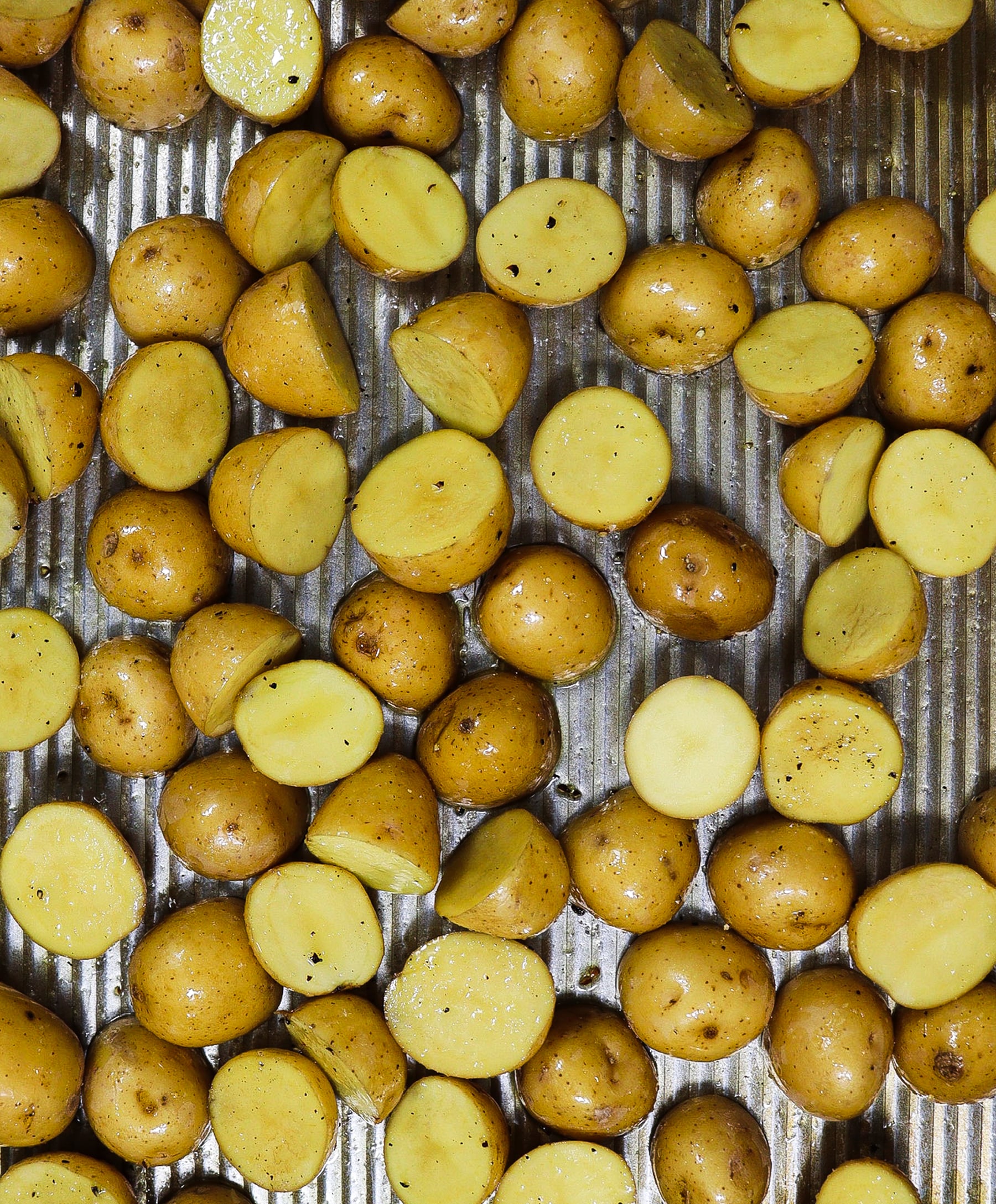 Baking sheet with baby potatoes cut in half tossed in olive oil, salt and pepper, ready to be baked