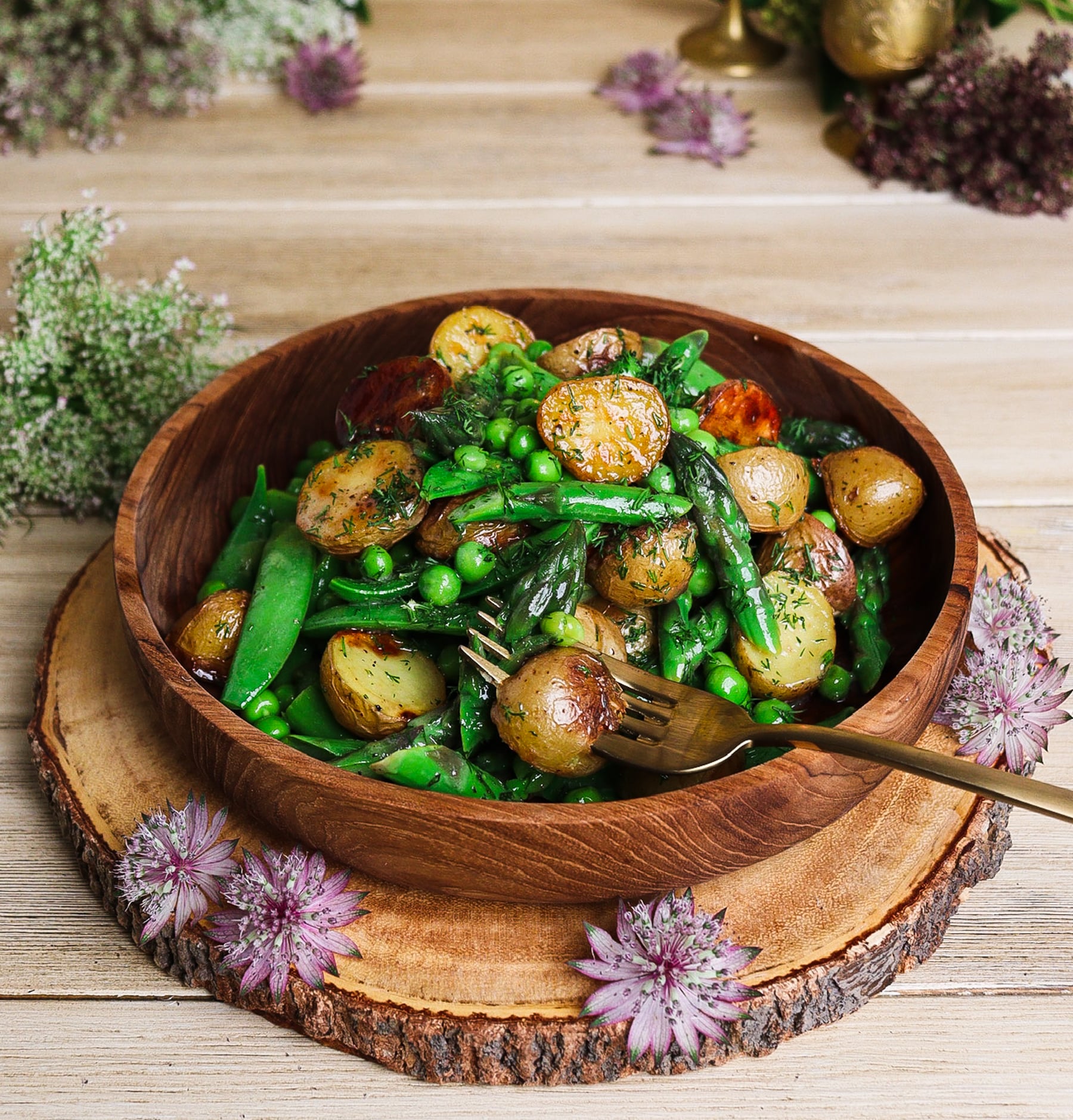 warm potato asparagus and pea salad in a rustic bowl surrounded by florals to evoke Lothlórien of Middle Earth