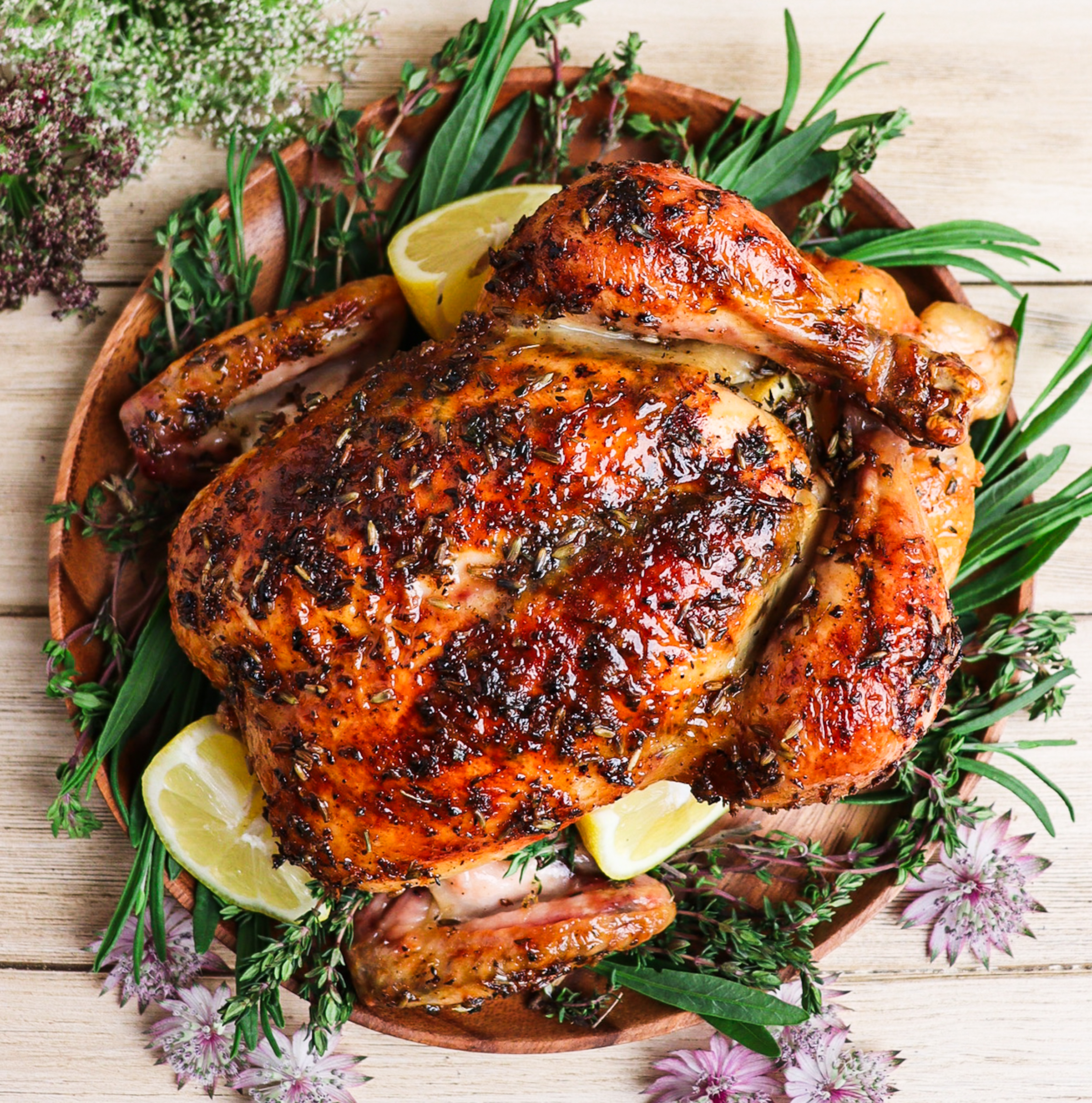 Top view of roast chicken glazed with honey and lavender surrounded by herbs and purple blossoms