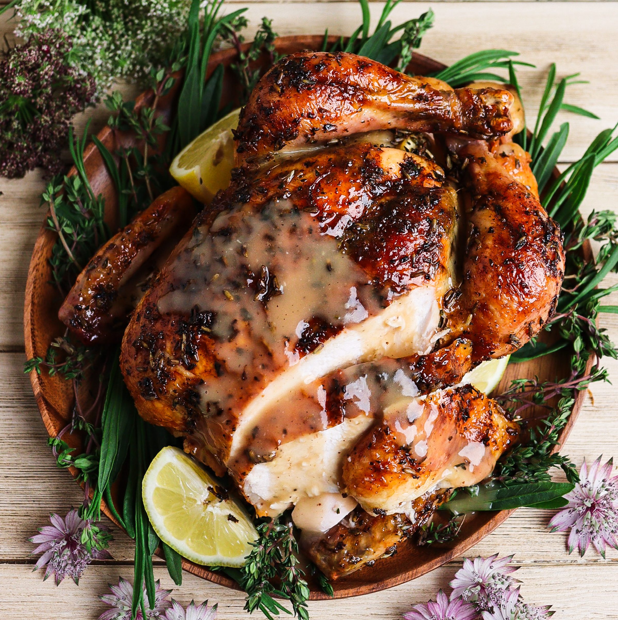 Roast chicken with honey lavender glaze and gravy styled with fresh herbs and purple flowers on a rustic plate