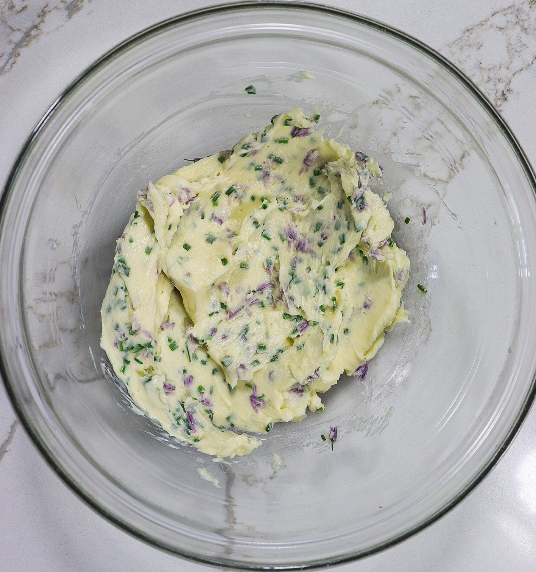 mixed butter chive blossoms and chives in a mixing bowl