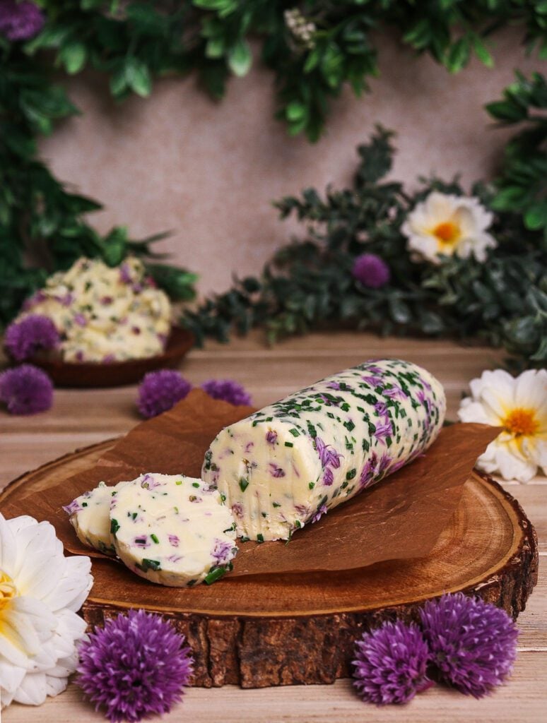 A log of chive blossom butter cut into slices on a rustic platter surrounded by flowers inspired by the elves of Middle Earth