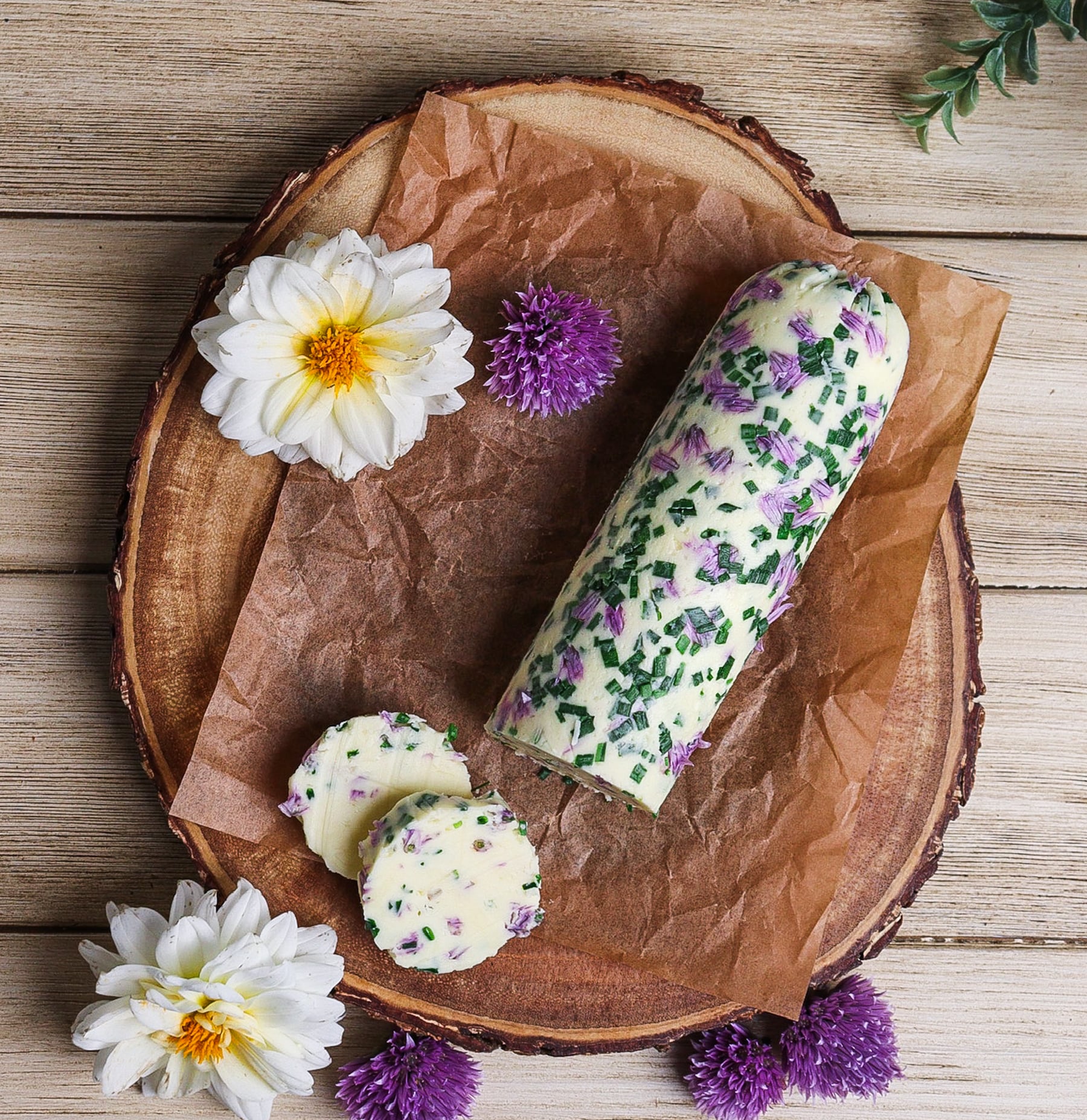 Top shot of chive blossom butter in a log roll on a rustic platter