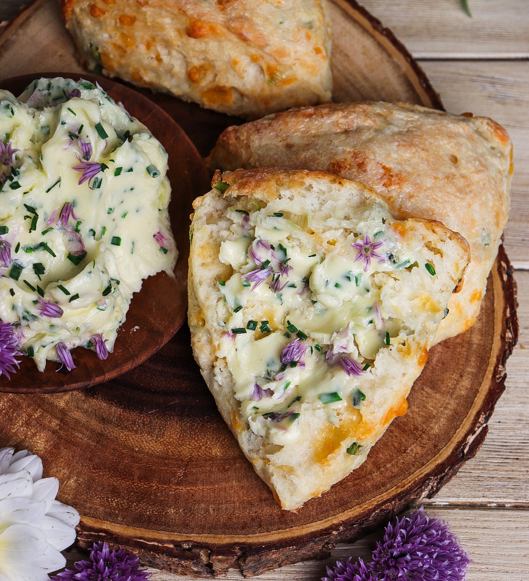 Cheddar, green onion and yogurt scone topped with chive blossom butter on a rustic plate