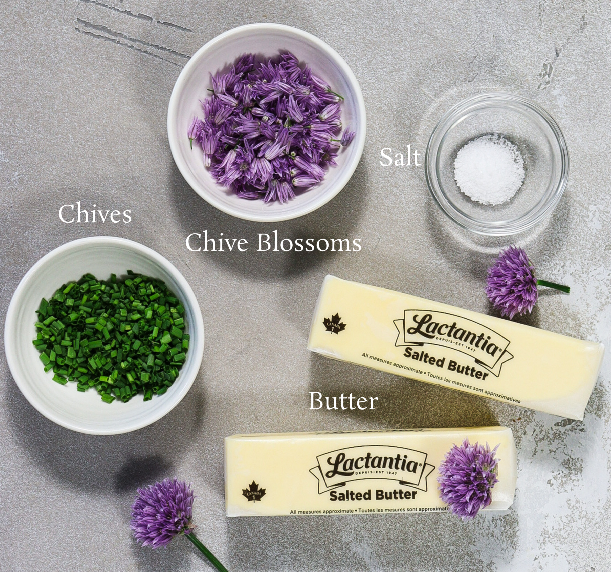 Ingredients for chive blossom butter including chive blossoms, cut chives, butter sticks and salt