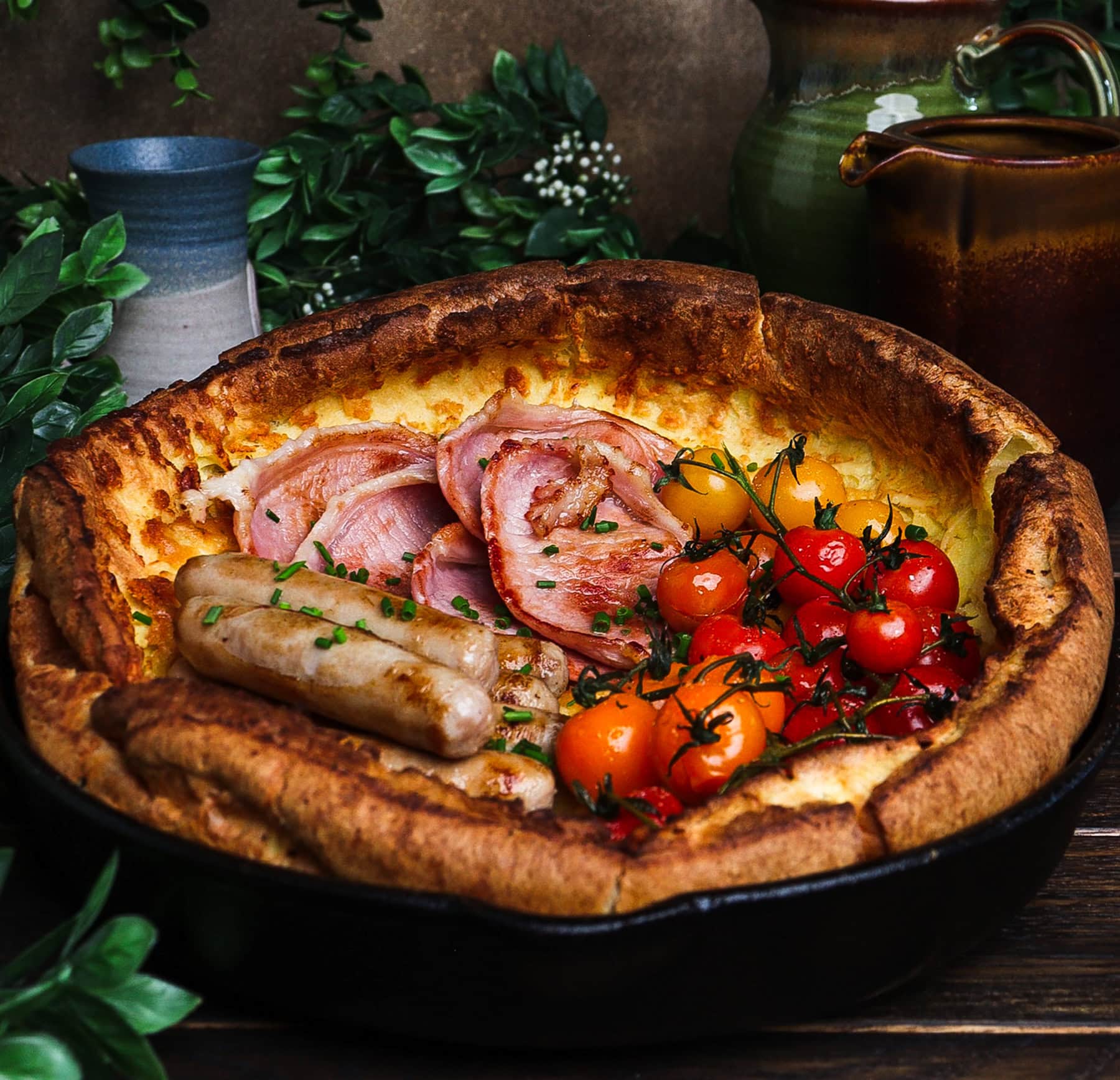 dutch baby in a skillet with bacon, sausages and tomatoes