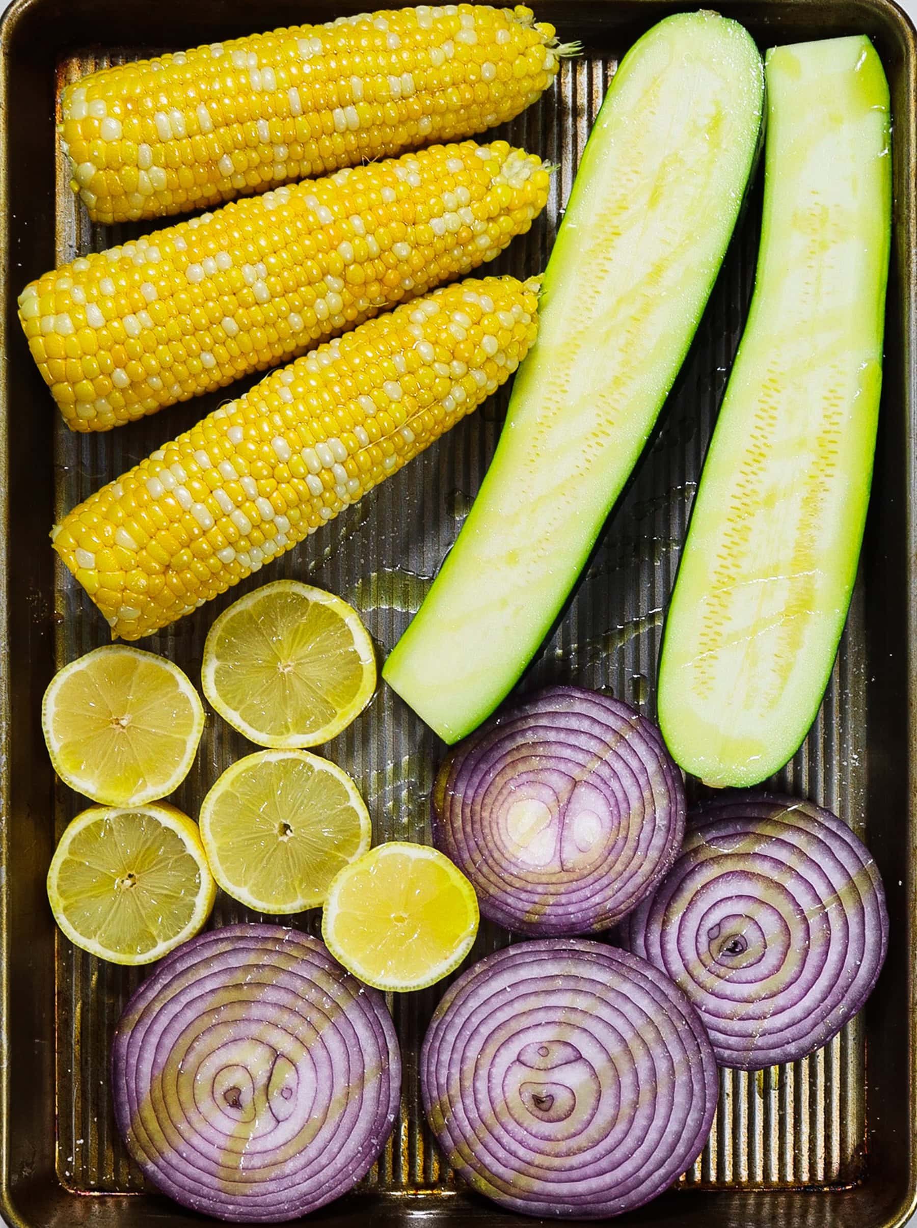 Corn cob, zucchini, lemon and onions on a sheet pan for grilling