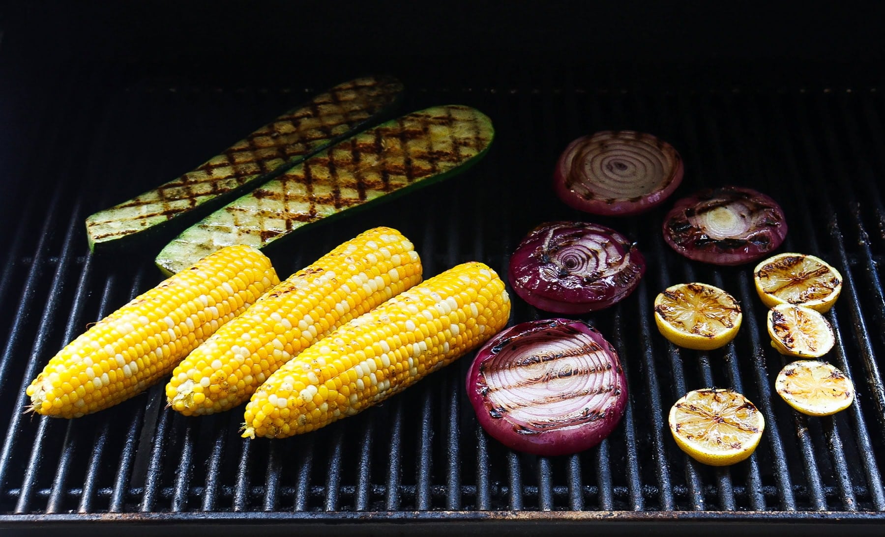 Corn cobs, zucchini, red onions and lemons grilling on a bbq