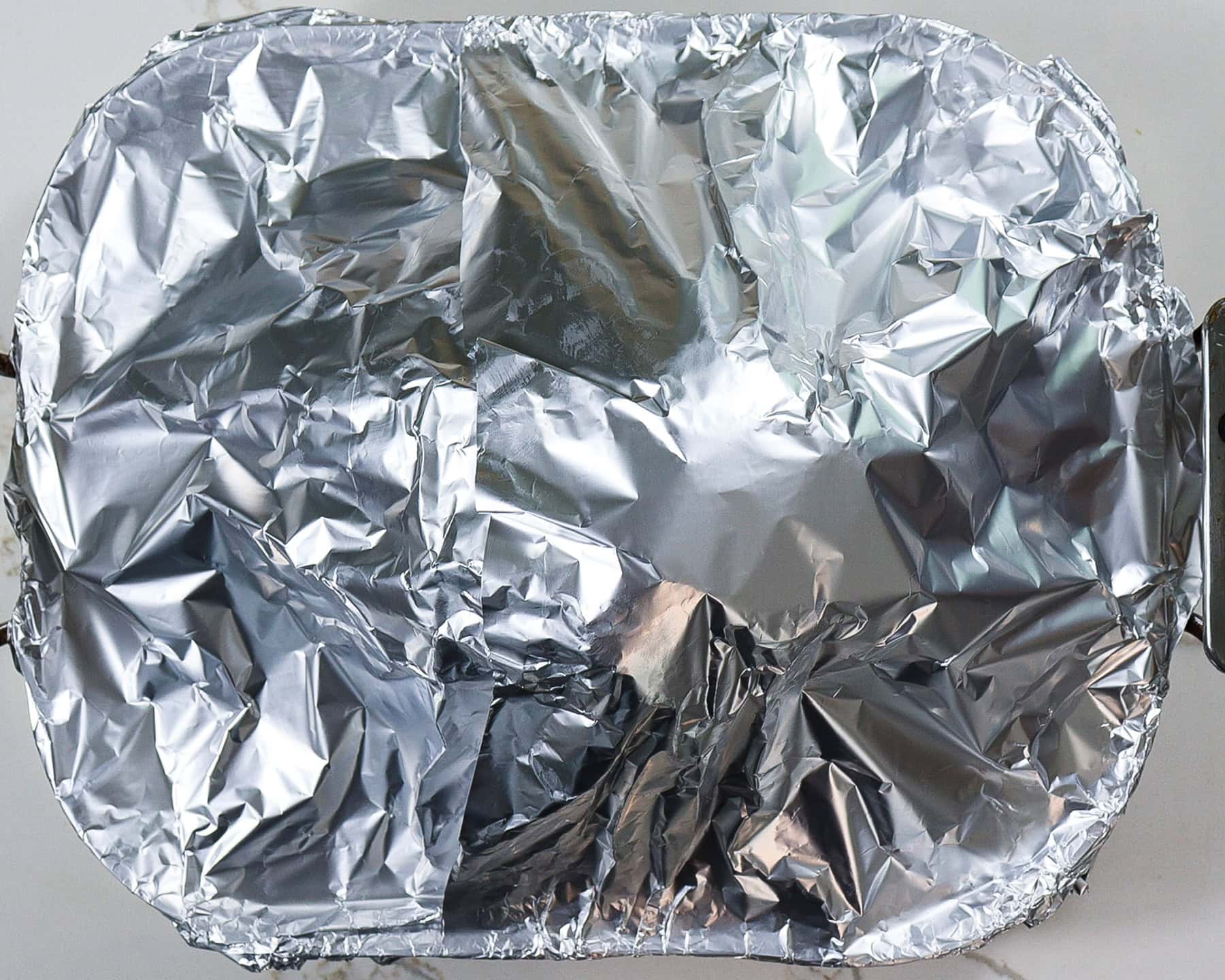 beer glazed ham in a roasting pan covered in parchment paper and foil