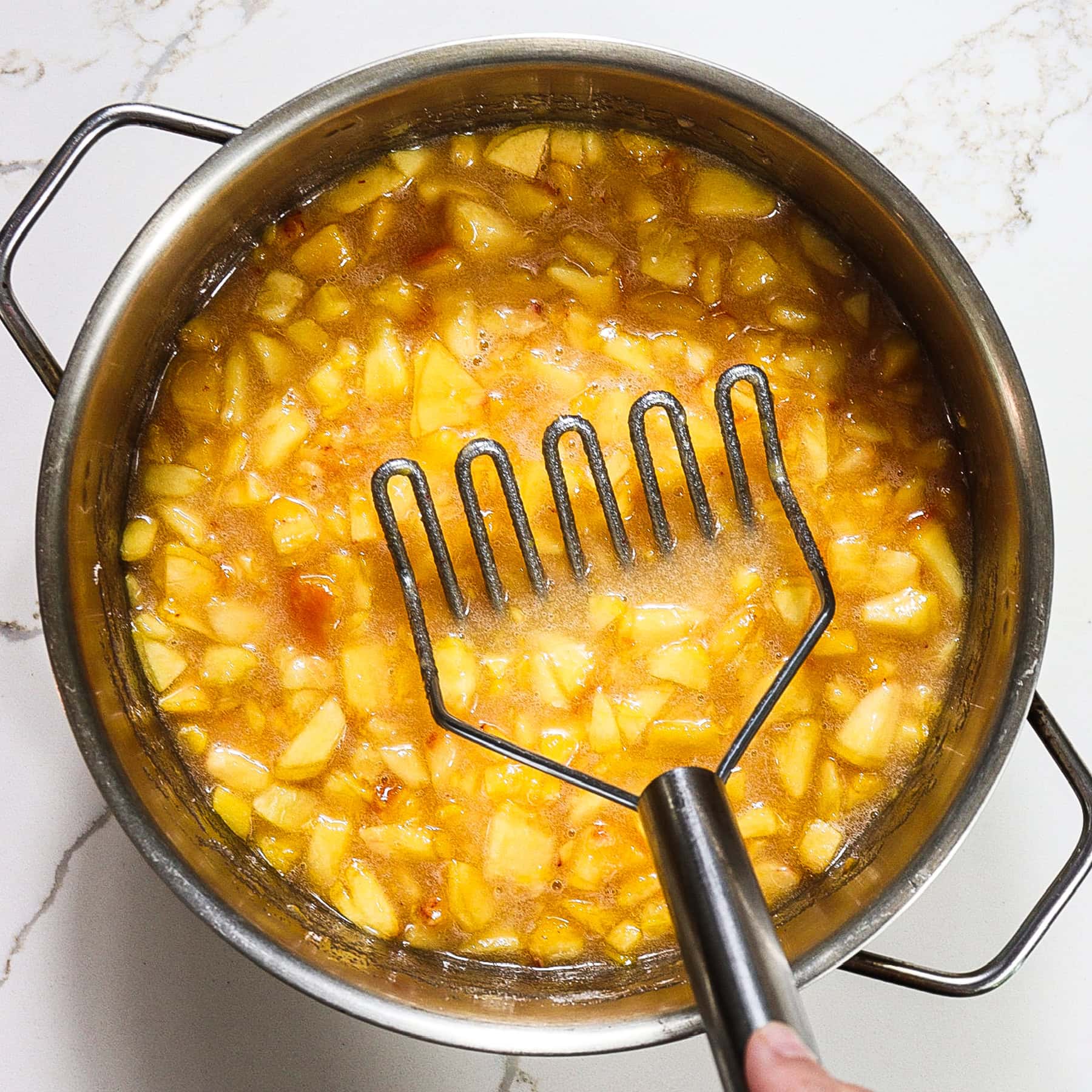 peaches in a pot with a masher 