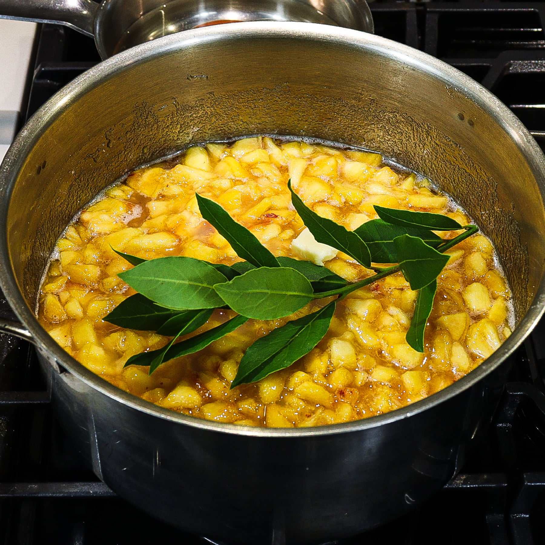 homemade peach jam cooking on a stove with fresh bay leaves