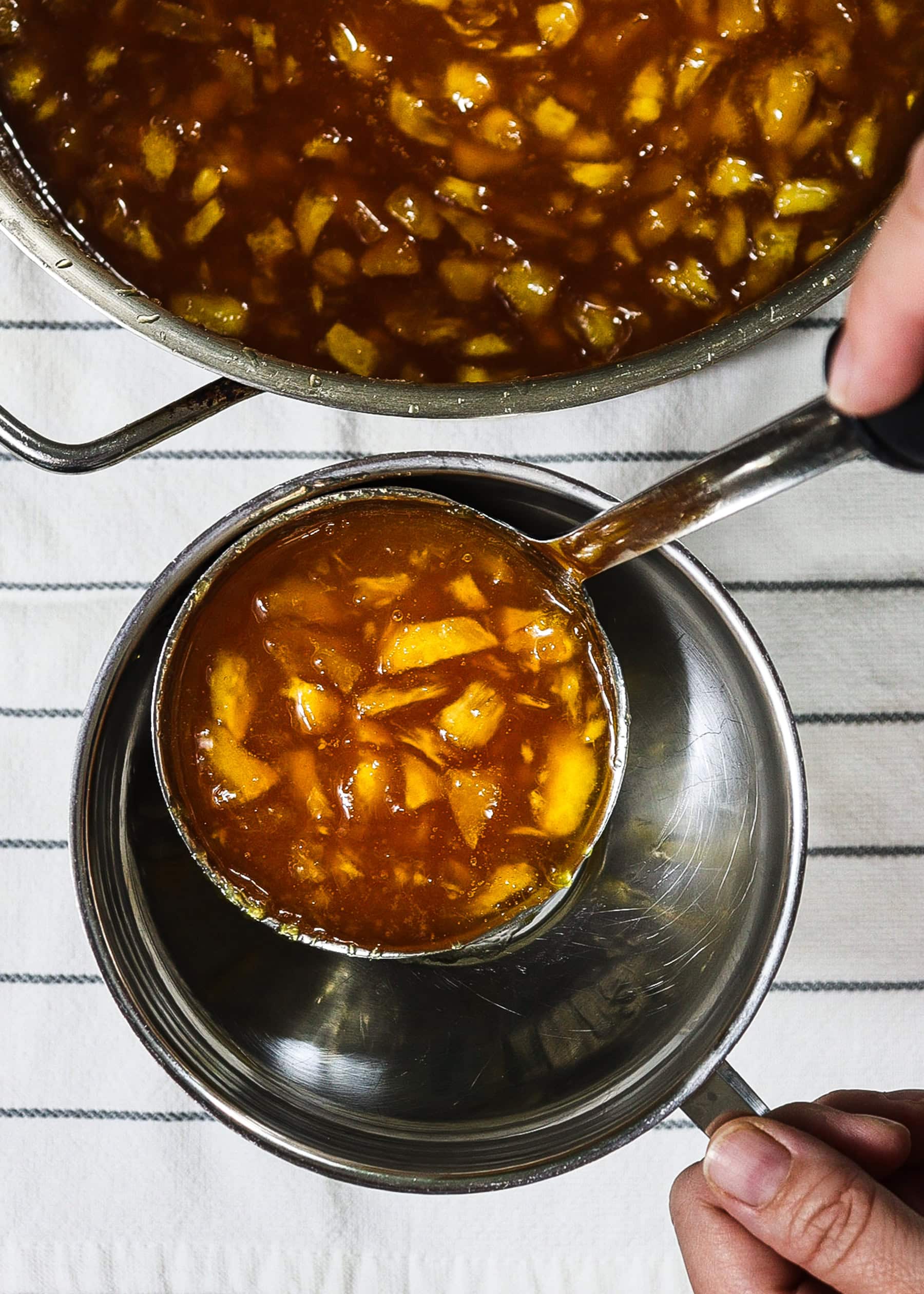 Ladling homemade peach jam into a har using a funnel