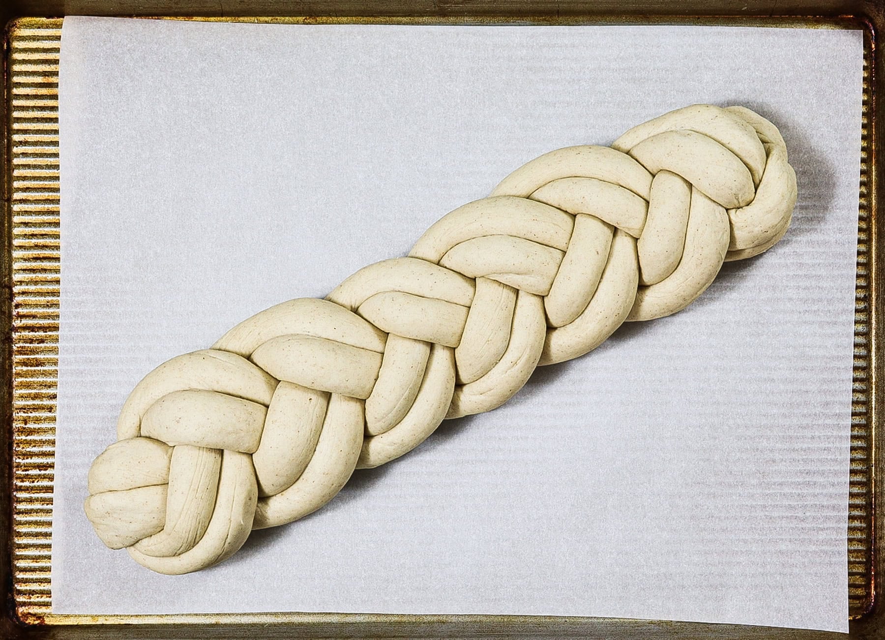 Double strand braided soft barley bread dough on a baking pan before baking