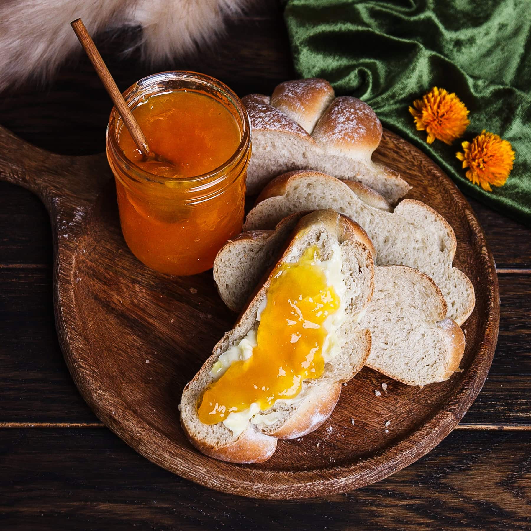 sliced soft barley bread spread with butter and peach and bay leaf jam on a rustic board