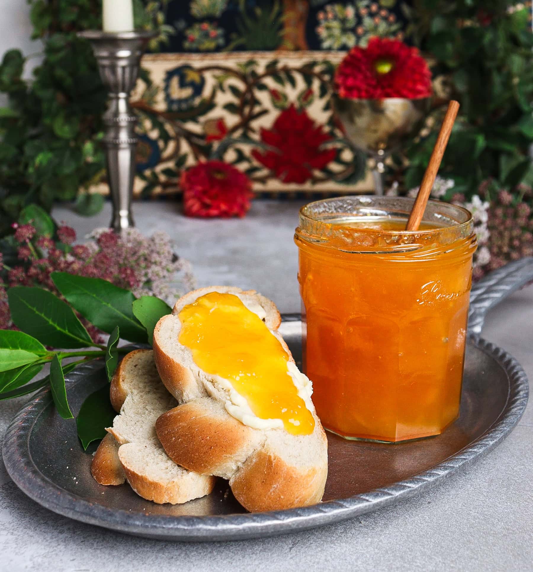 Jar of peach and bay leaf jam and slices of bread with butter and peach jam