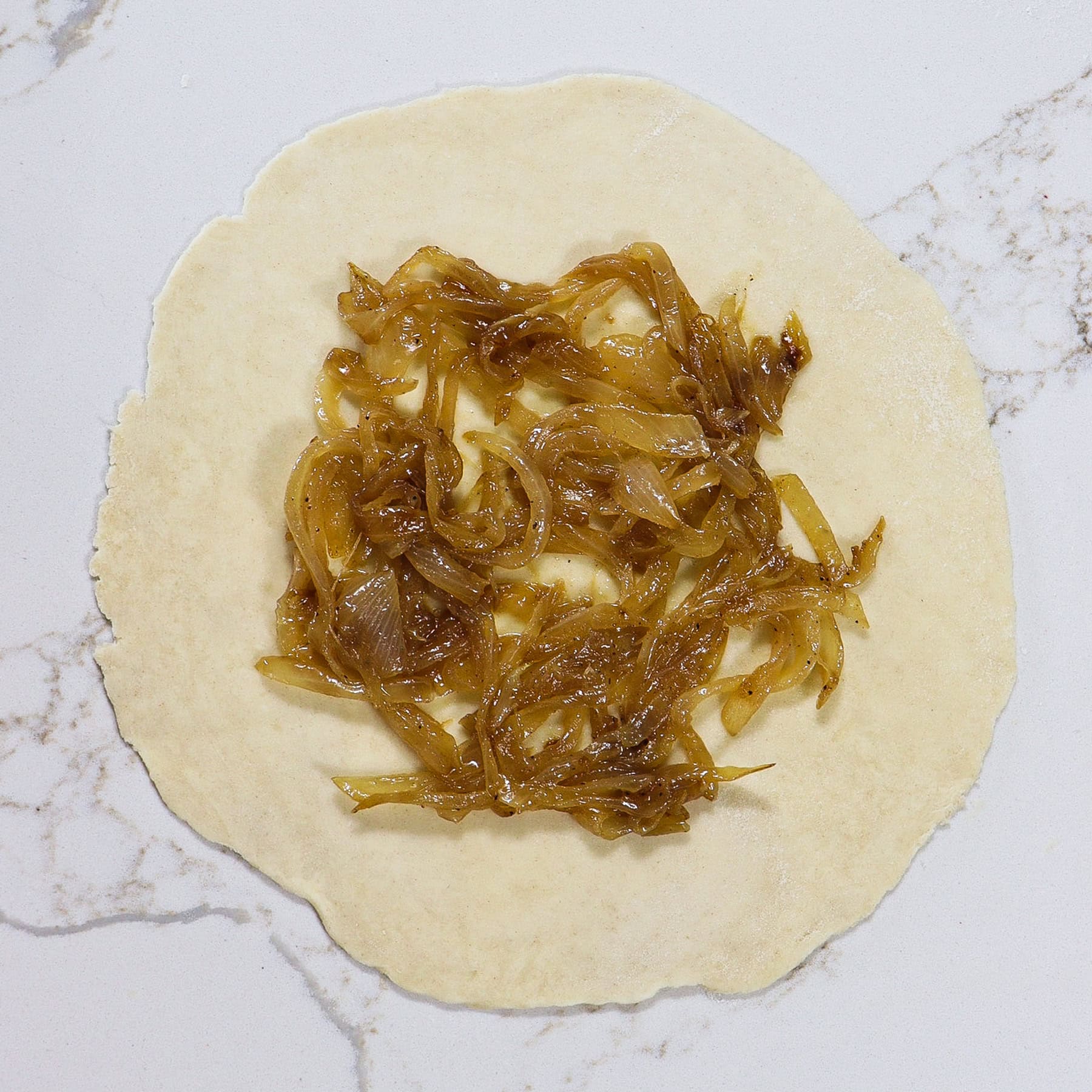 pie dough in a circle topped with caramelized onions