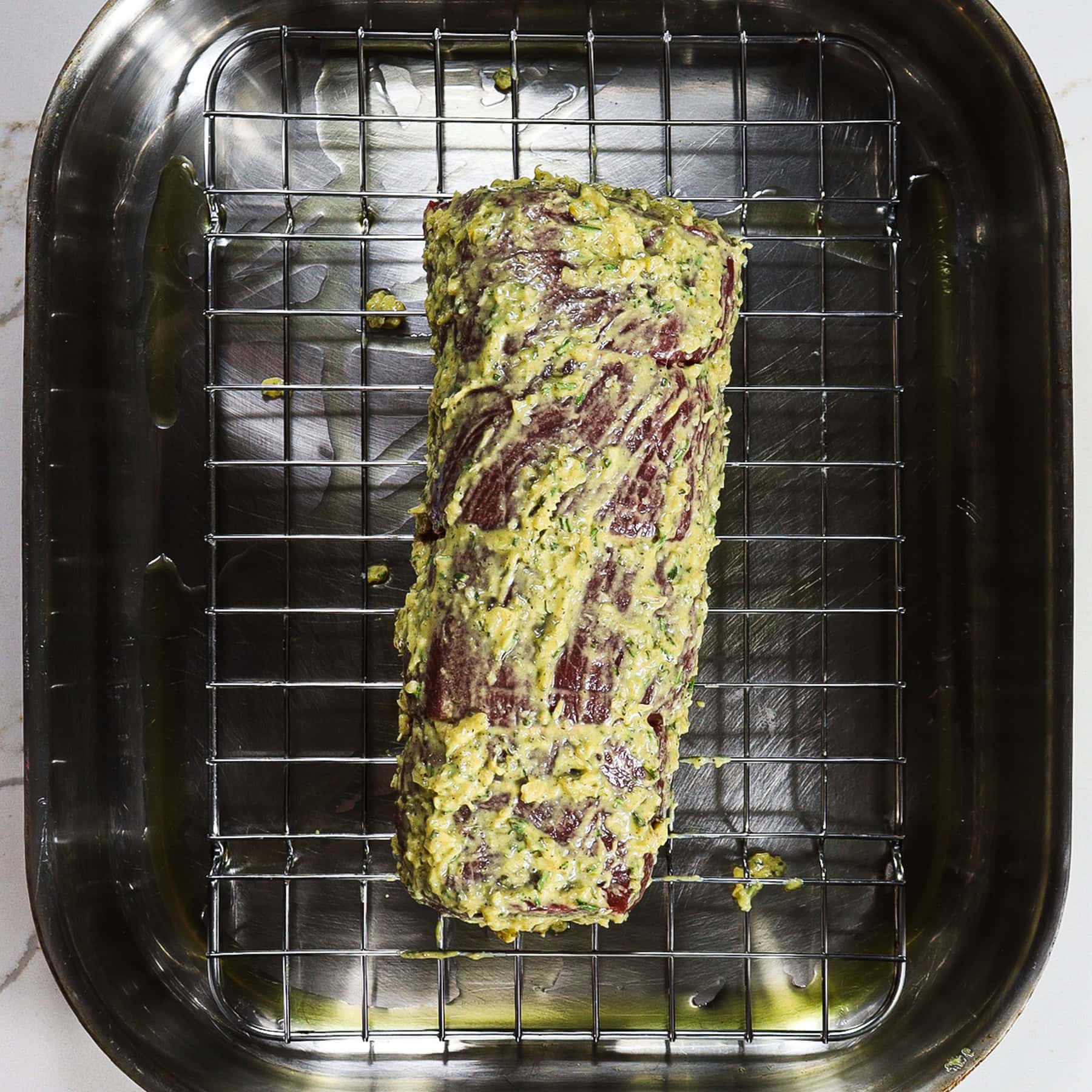 uncooked beef tenderloin covered in horseradish marinade on a roasting pan