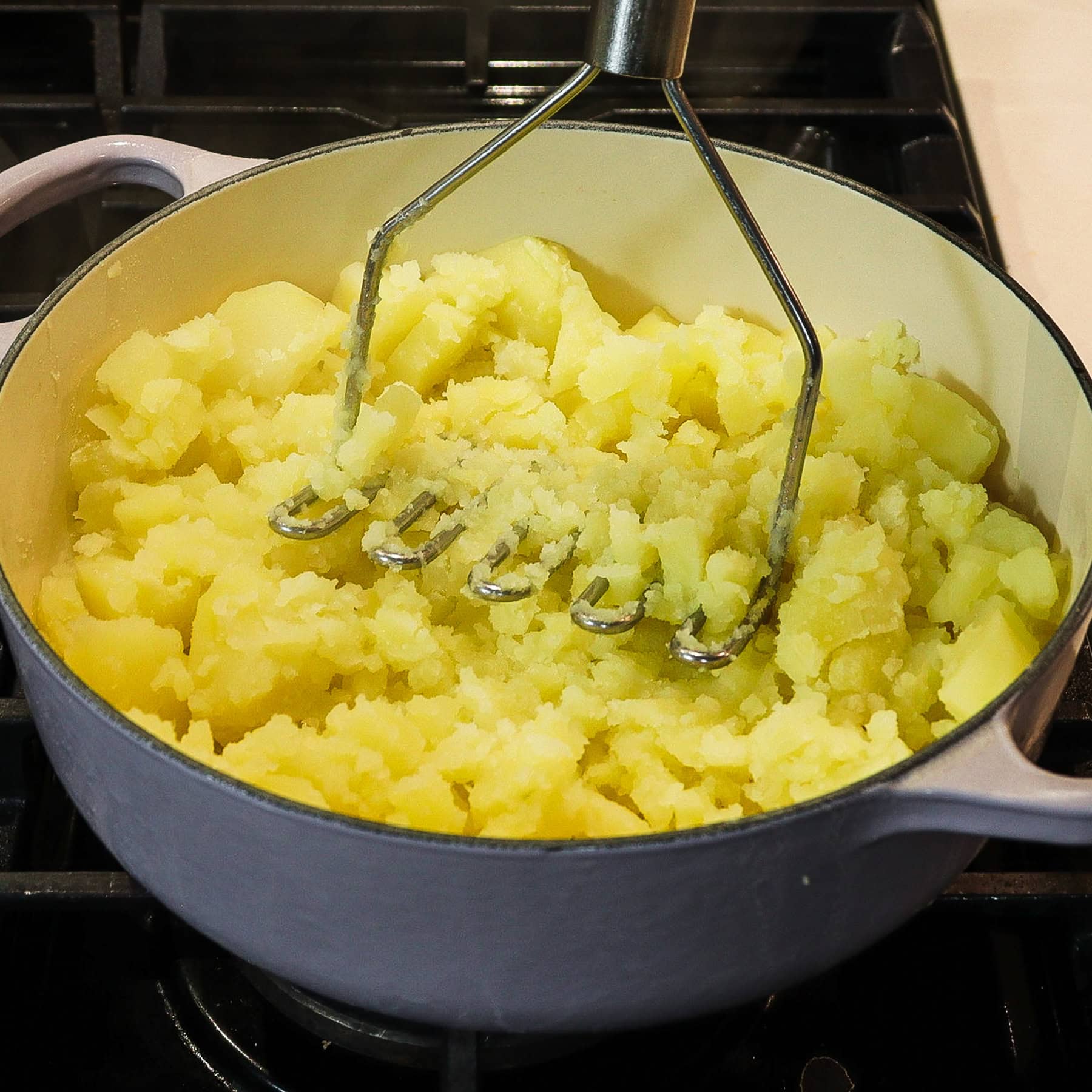 potato masher in a pot of partly mashed potatoes