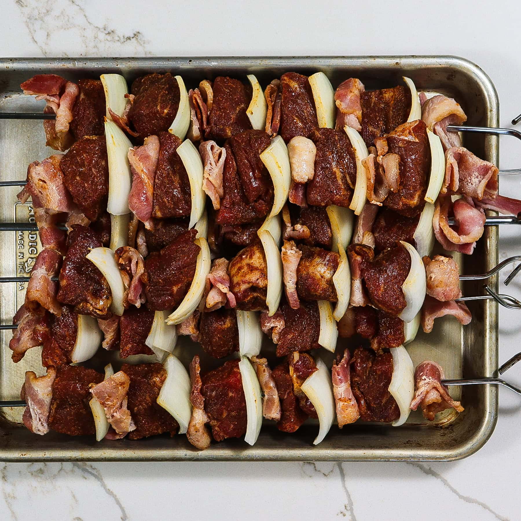 steak, bacon and onion skewers on a sheet pan before grilling