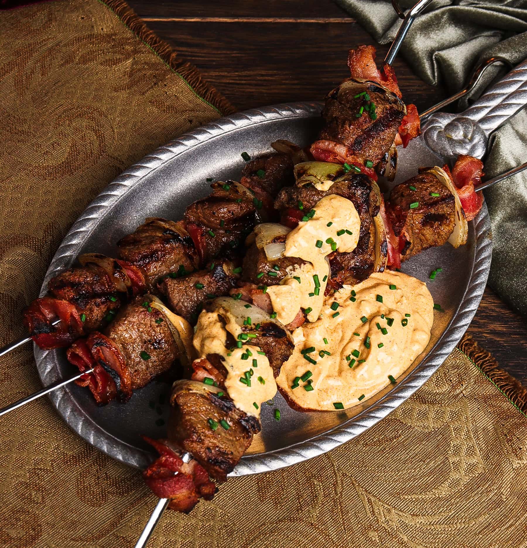 skewers of robber steak skewers on a pewter plate with garlic and paprika cream sauce
