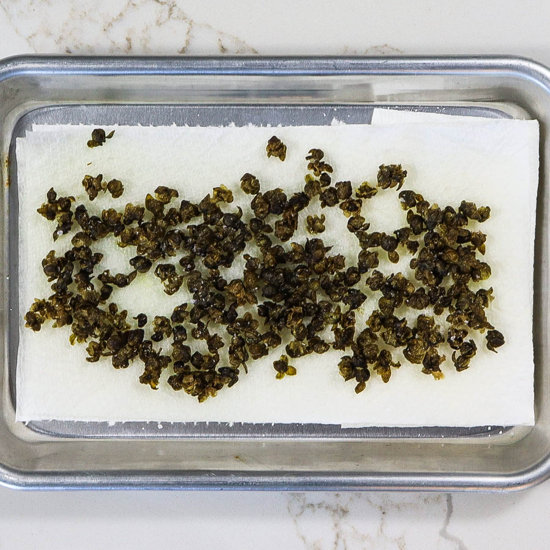 crispy fried capers drying on a paper towel-lined sheet pan