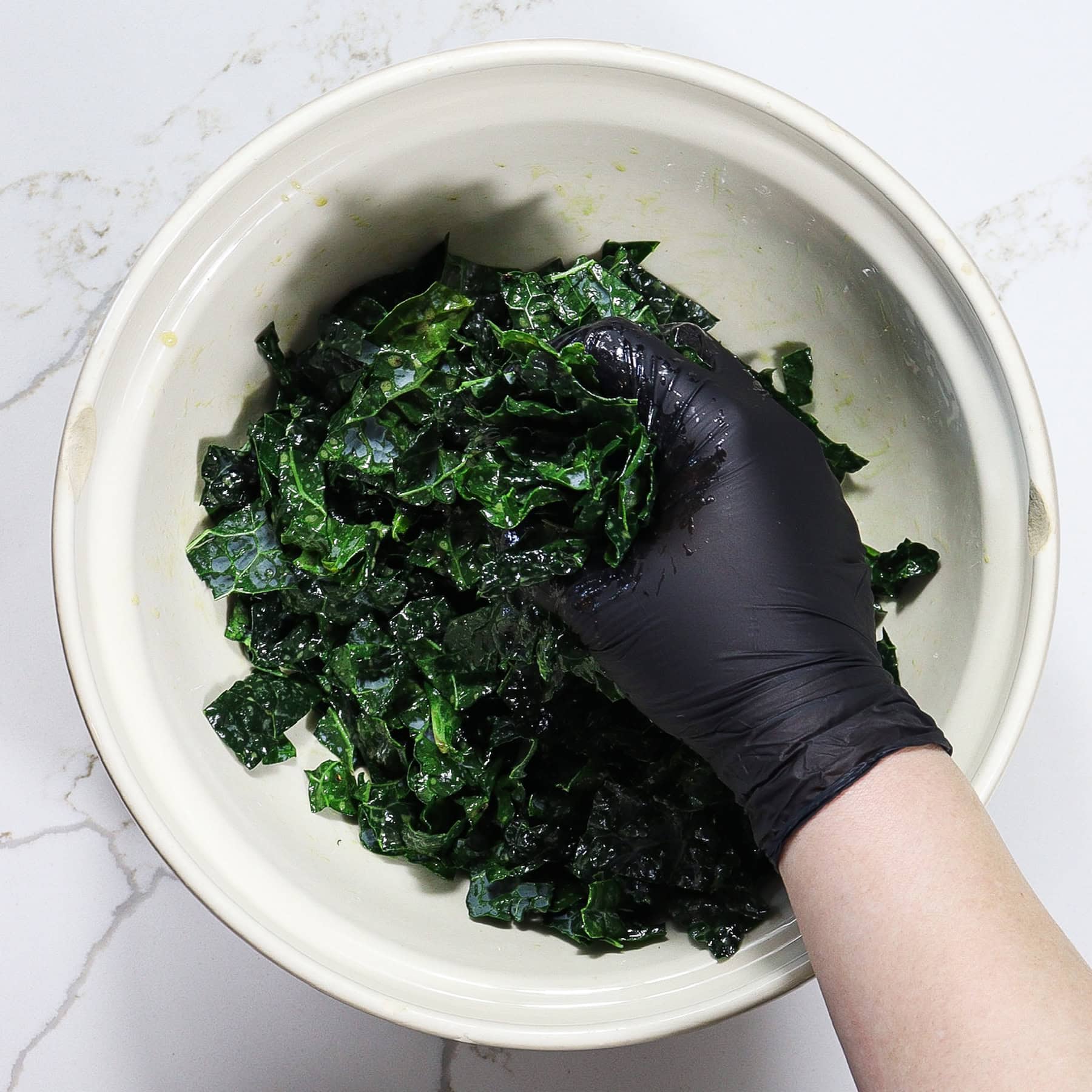 massaging kale with vinaigrette in a mixing bowl